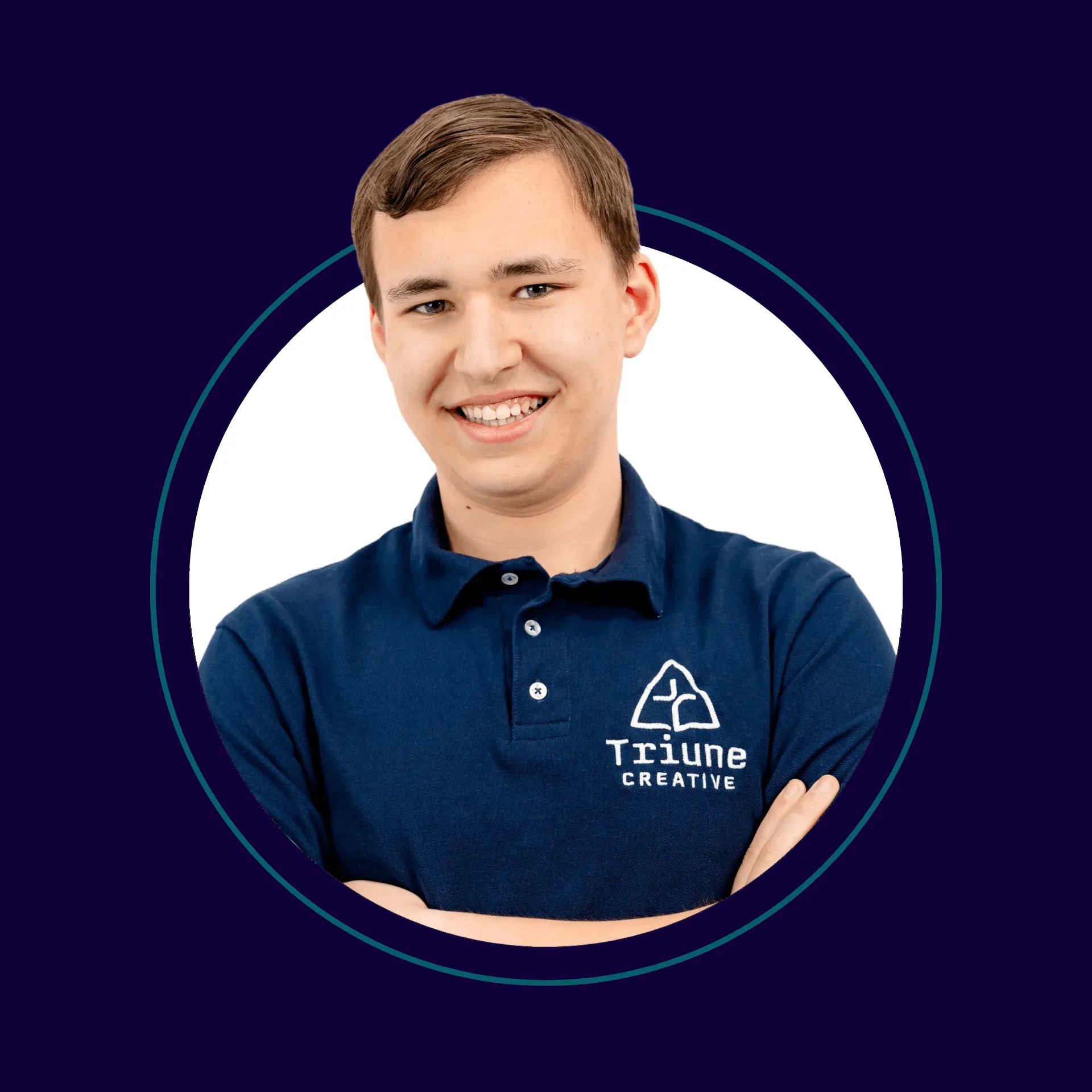 A young man with short brown hair, smiling and crossing his arms, wearing a navy blue polo shirt with a logo that says 'Triune Creative'.